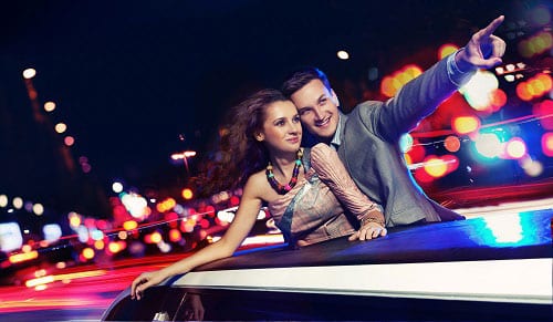 Couple in limousine standing up through the moon roof looking at the city.